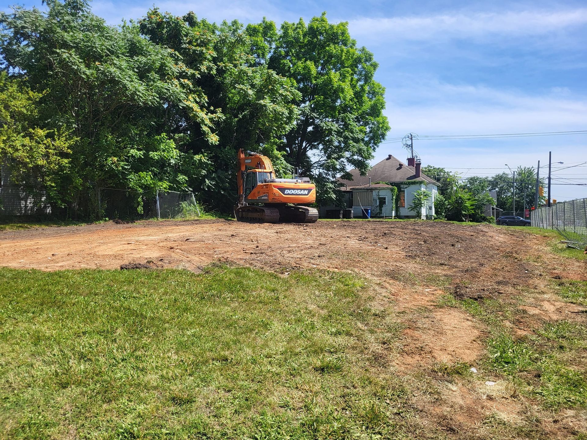 A large orange excavator is sitting in the middle of a grassy field.