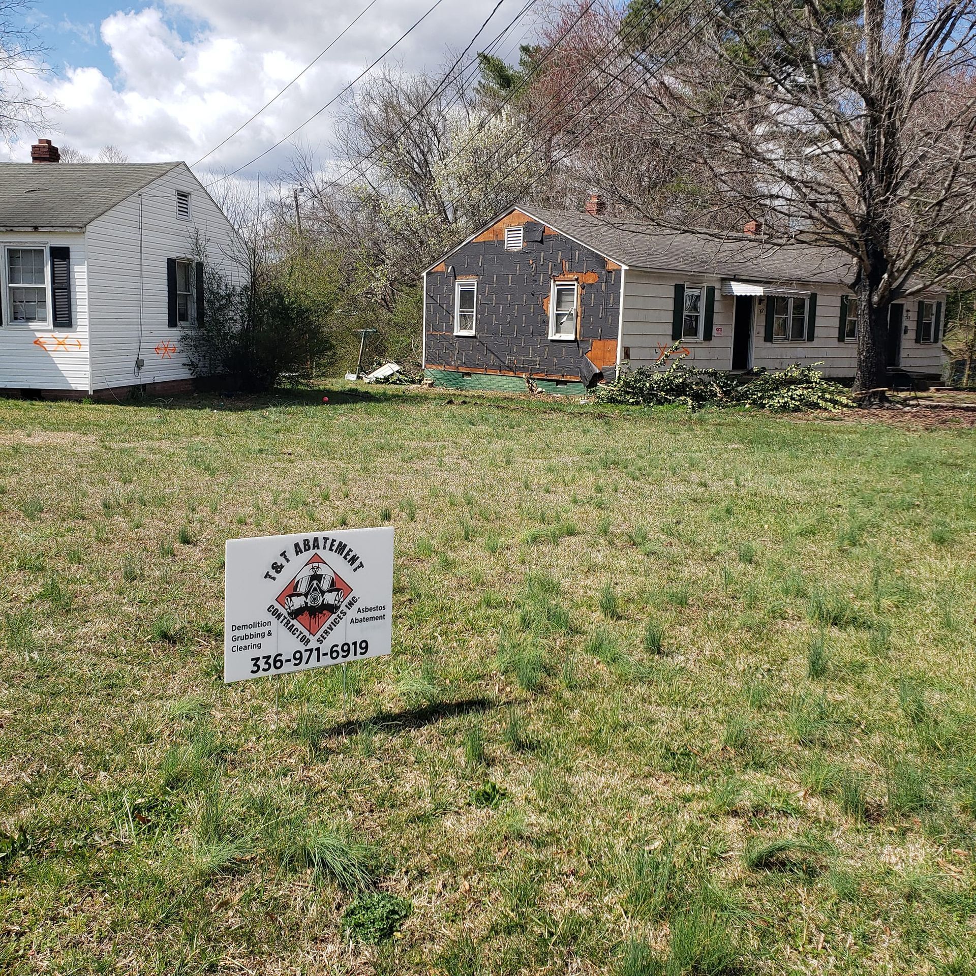 A sign in a grassy field with a house in the background.