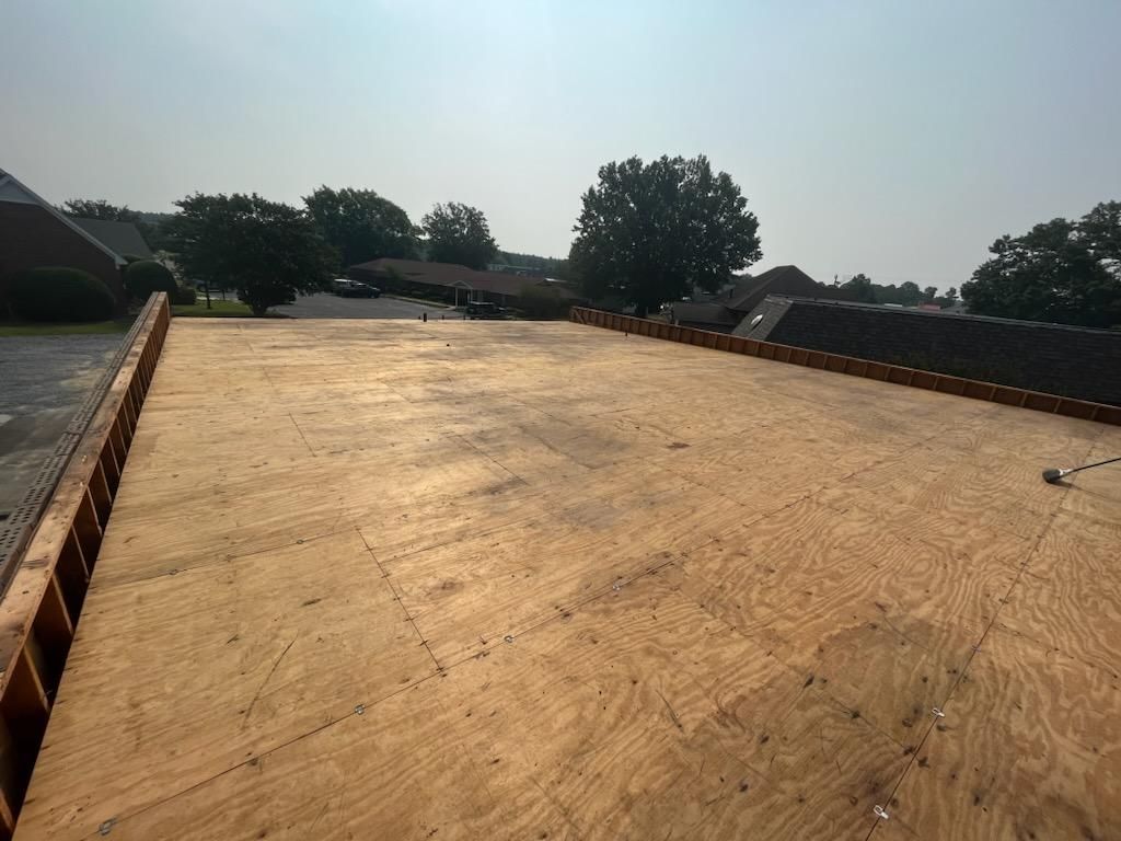 A roof with a lot of plywood on it and a lot of trees in the background.