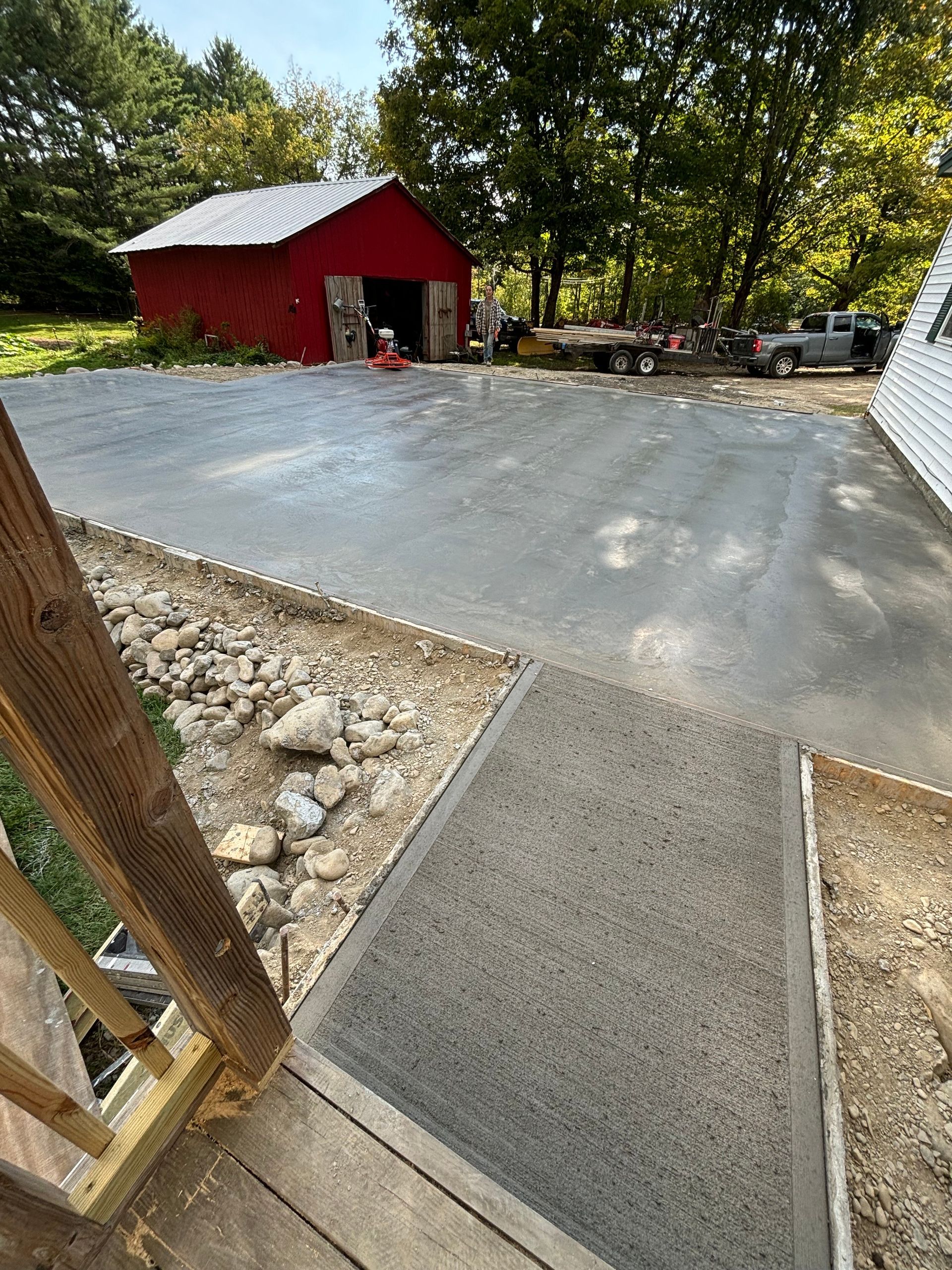 A concrete driveway is being built in front of a red barn.