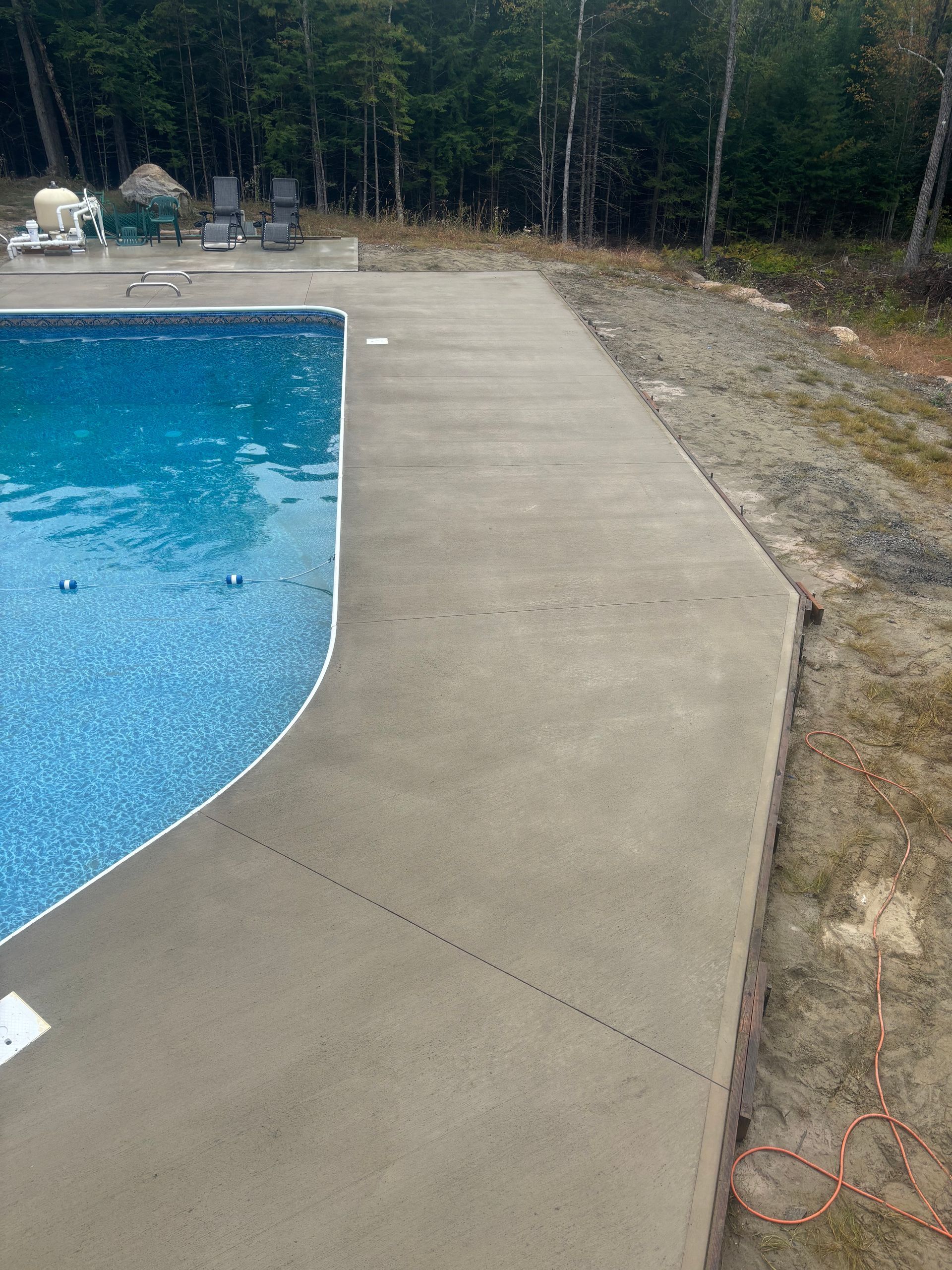 A concrete walkway leading to a swimming pool surrounded by trees.