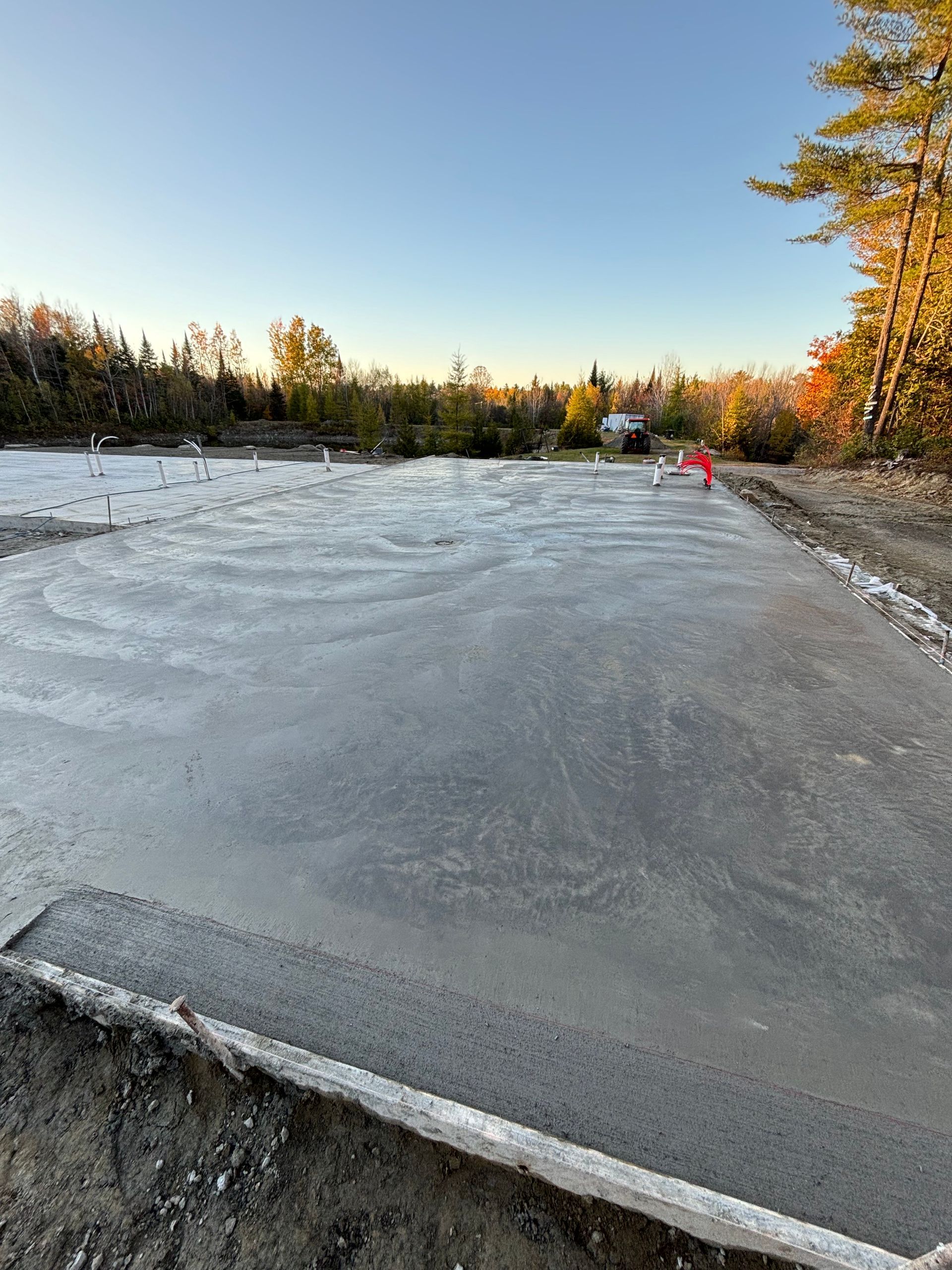 A concrete foundation is being built in a field with trees in the background.
