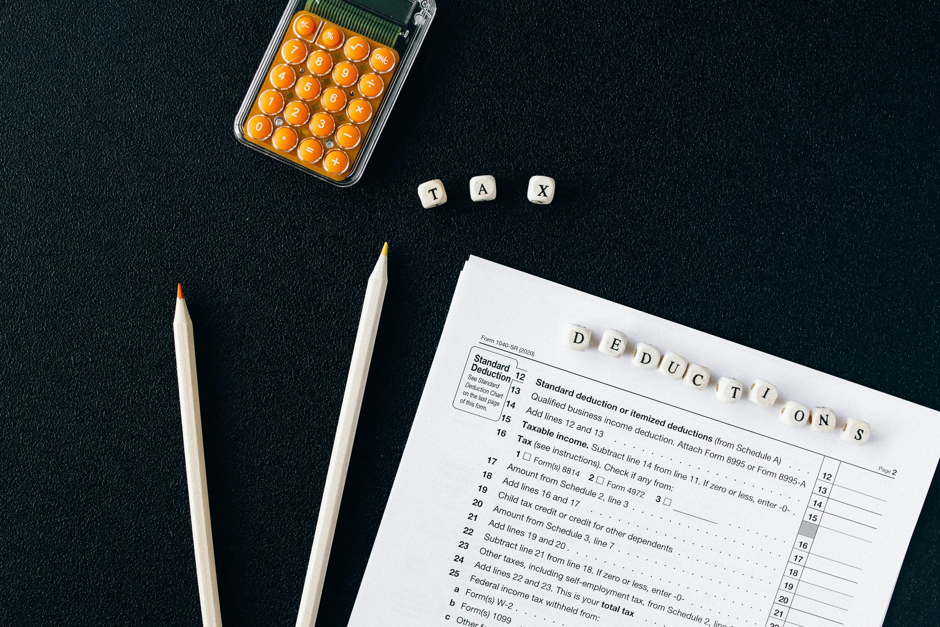 Pencil, pen, dice, and a checklist on a dark desk with an orange bead tray