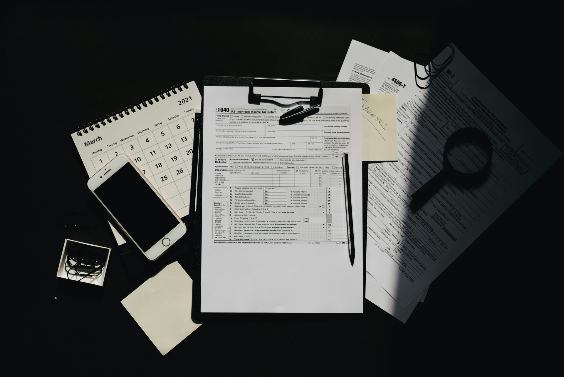 Desk with clipboard, pen, calculator, phone, and scattered papers under dim lighting