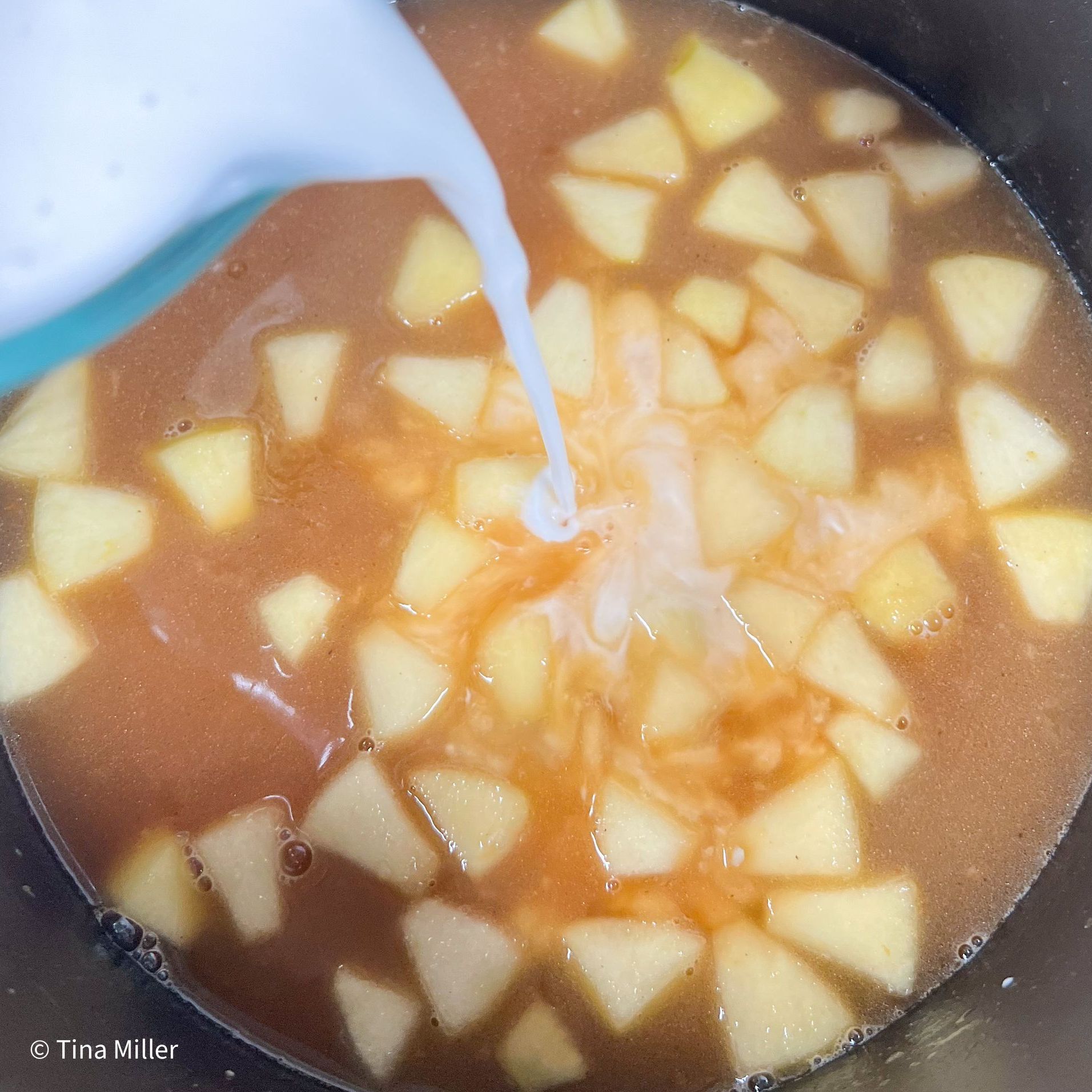 Apples in Dutch oven simmering in vegetable broth while adding coconut milk to the pot. 