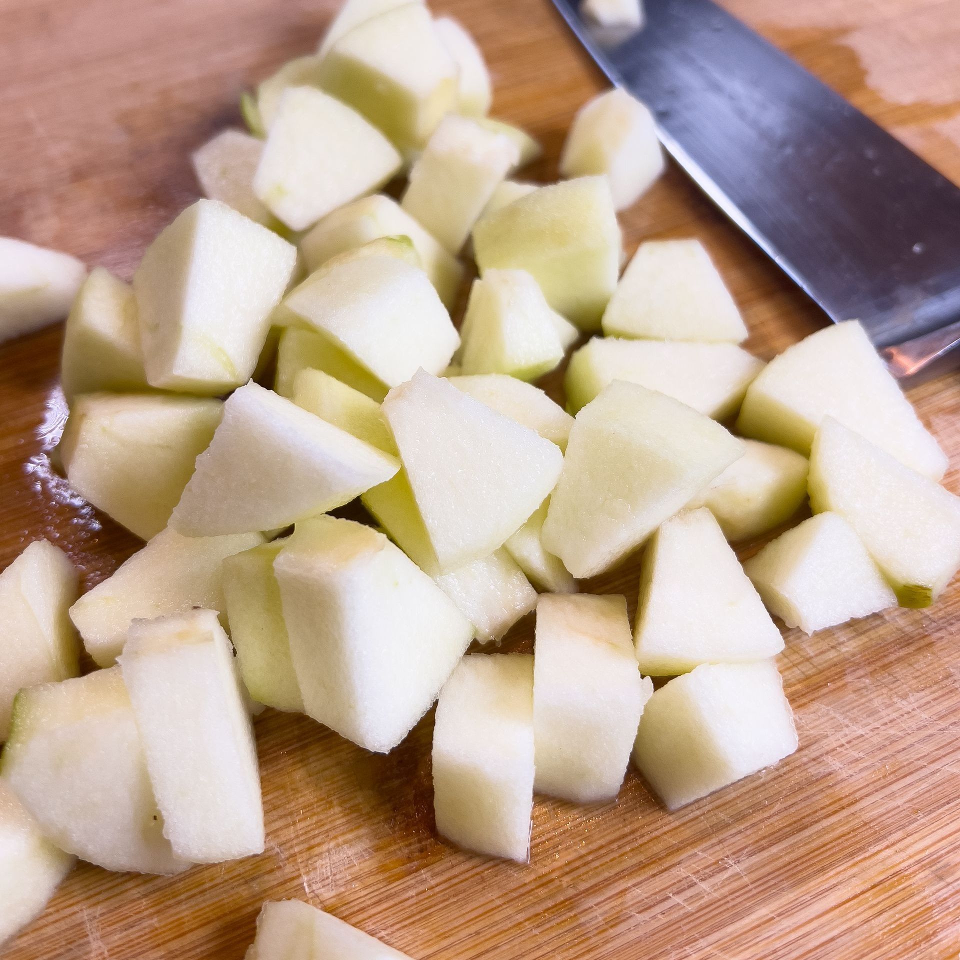 Granny Smith apples chopped on a cutting board with a knife in the background.