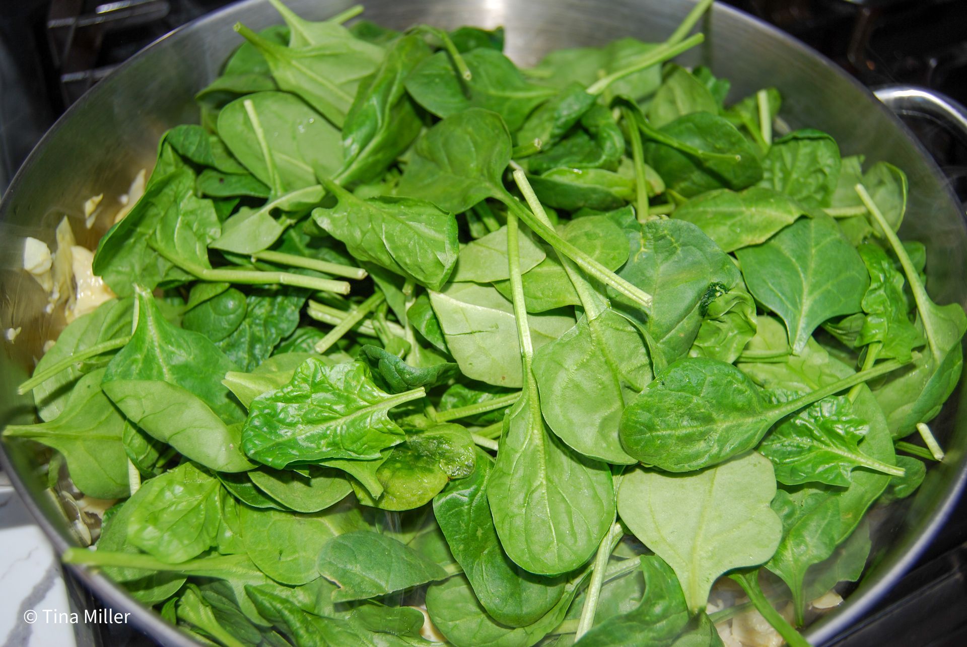Fresh spinach in a hot pan to wilt as part of spinach and artichoke dip.