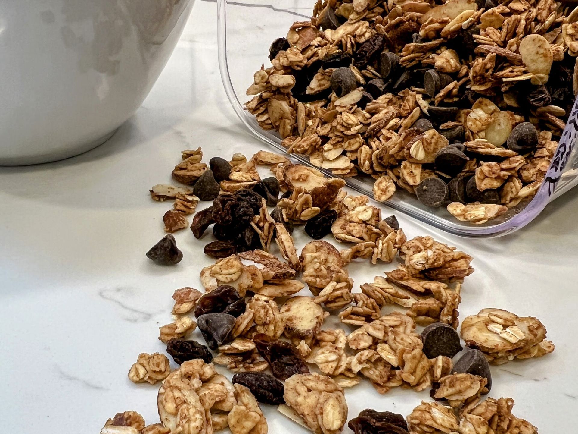 Almond butter granola with raisins and dark chocolate morsels laying on white marble countertop. 