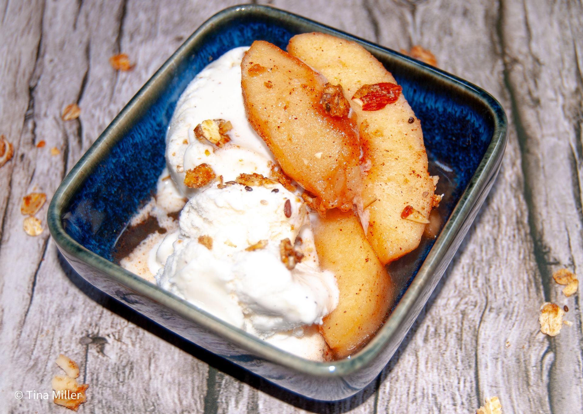 Cooked crockpot cinnamon apples in a small dessert dish with two scoops of vanilla ice cream, topped with granola.