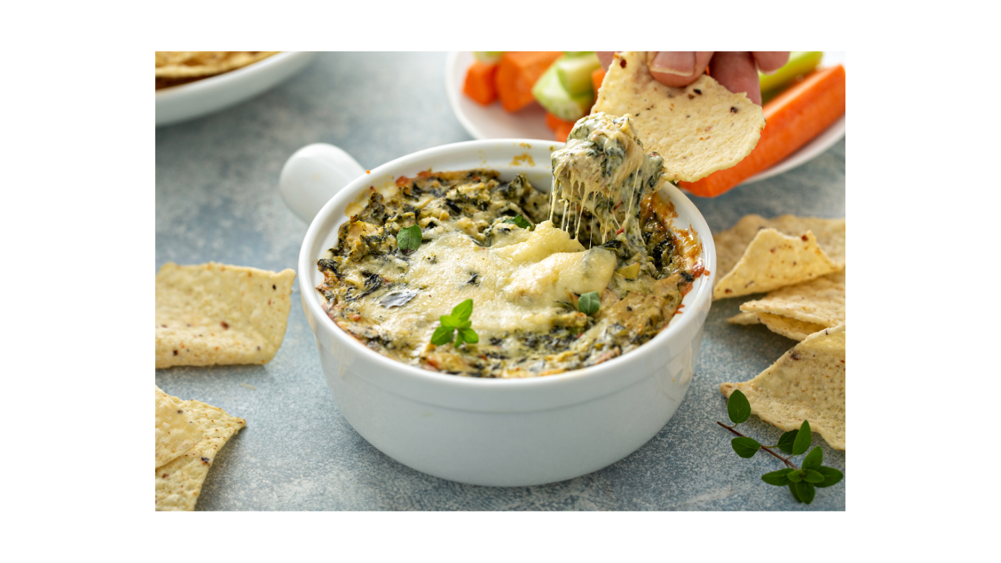 Spinach and artichoke dip in a small white ramekin with corn chips surrounding the bowl.