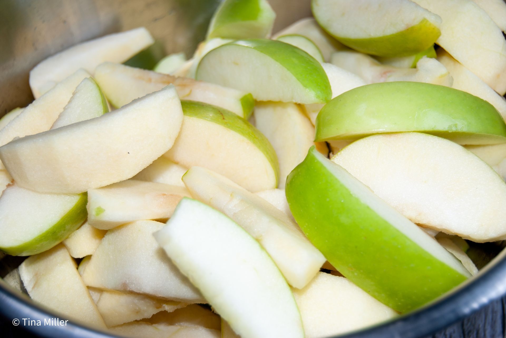 Granny Smith apples slices with skins left on some, piled high inside a crockpot.