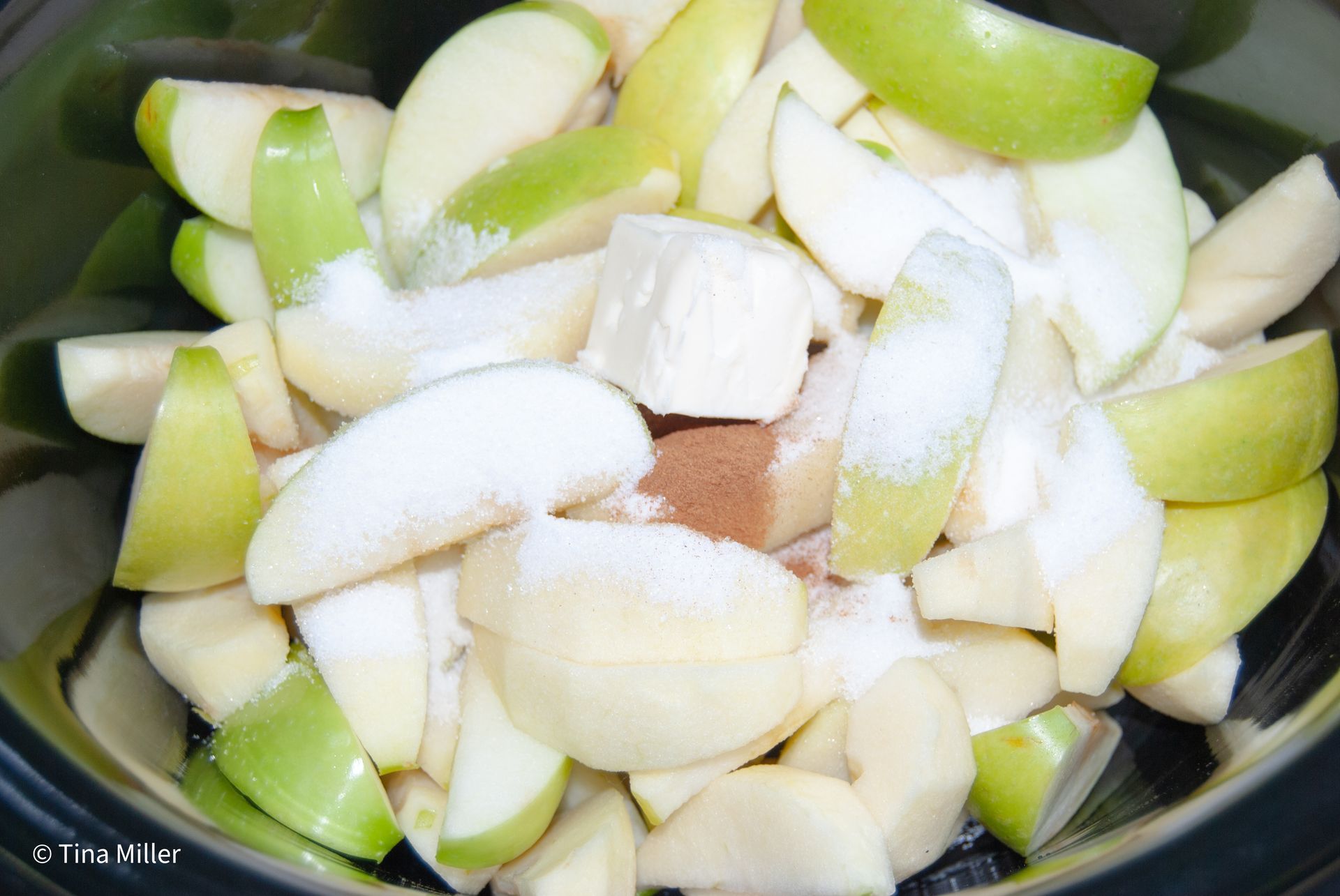 Granny Smith apples slices with skins left on some, piled high inside a crockpot topped with sugar, butter, kahlua, and cinnamon.
