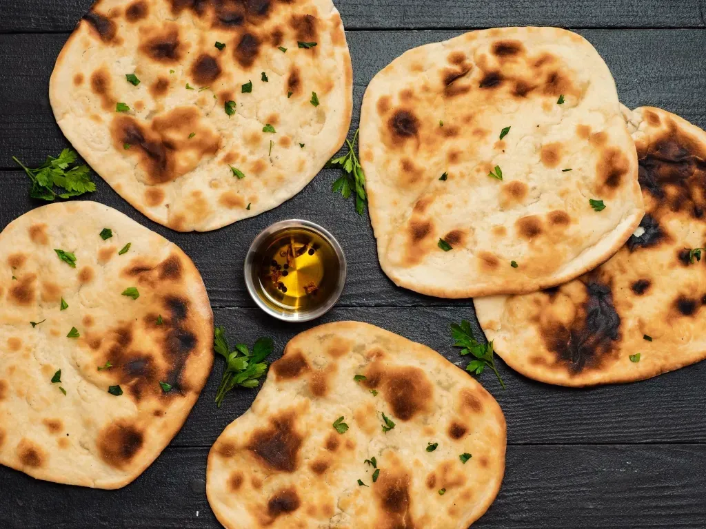 Grilled flatbreads laying flat on a dark surface layered with a small bowl of seasoned dipping oil.