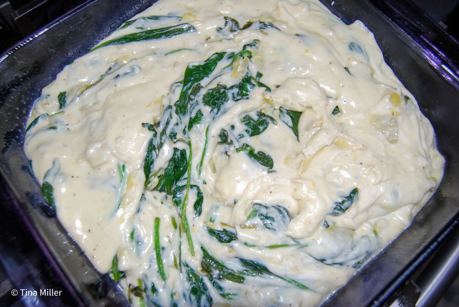 Spinach and artichoke dip poured into a 9x9 casserole dish before backing in the oven.