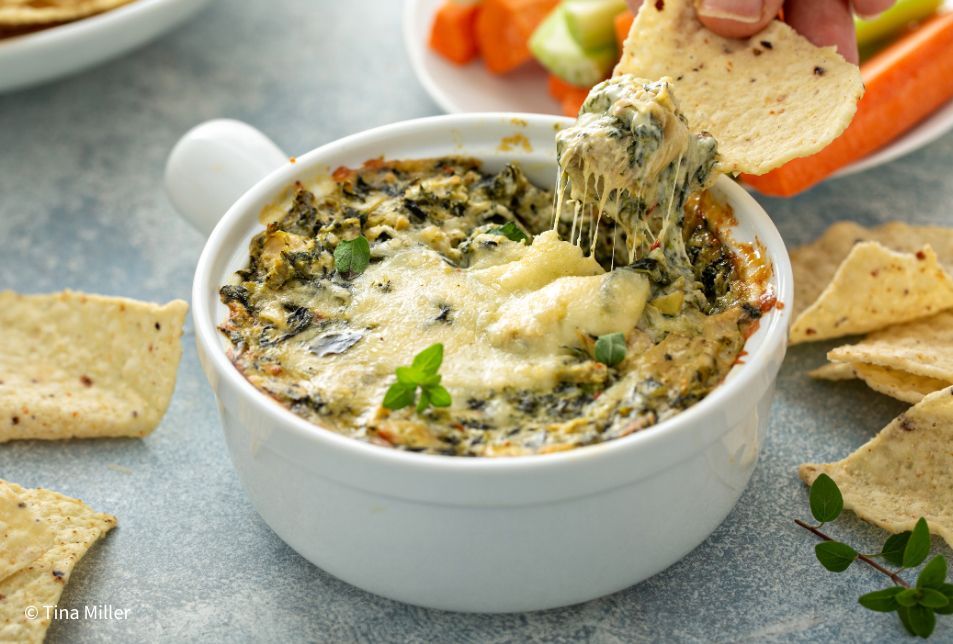 Spinach and artichoke dip in a small white ramekin with corn chips surrounding the bowl. 