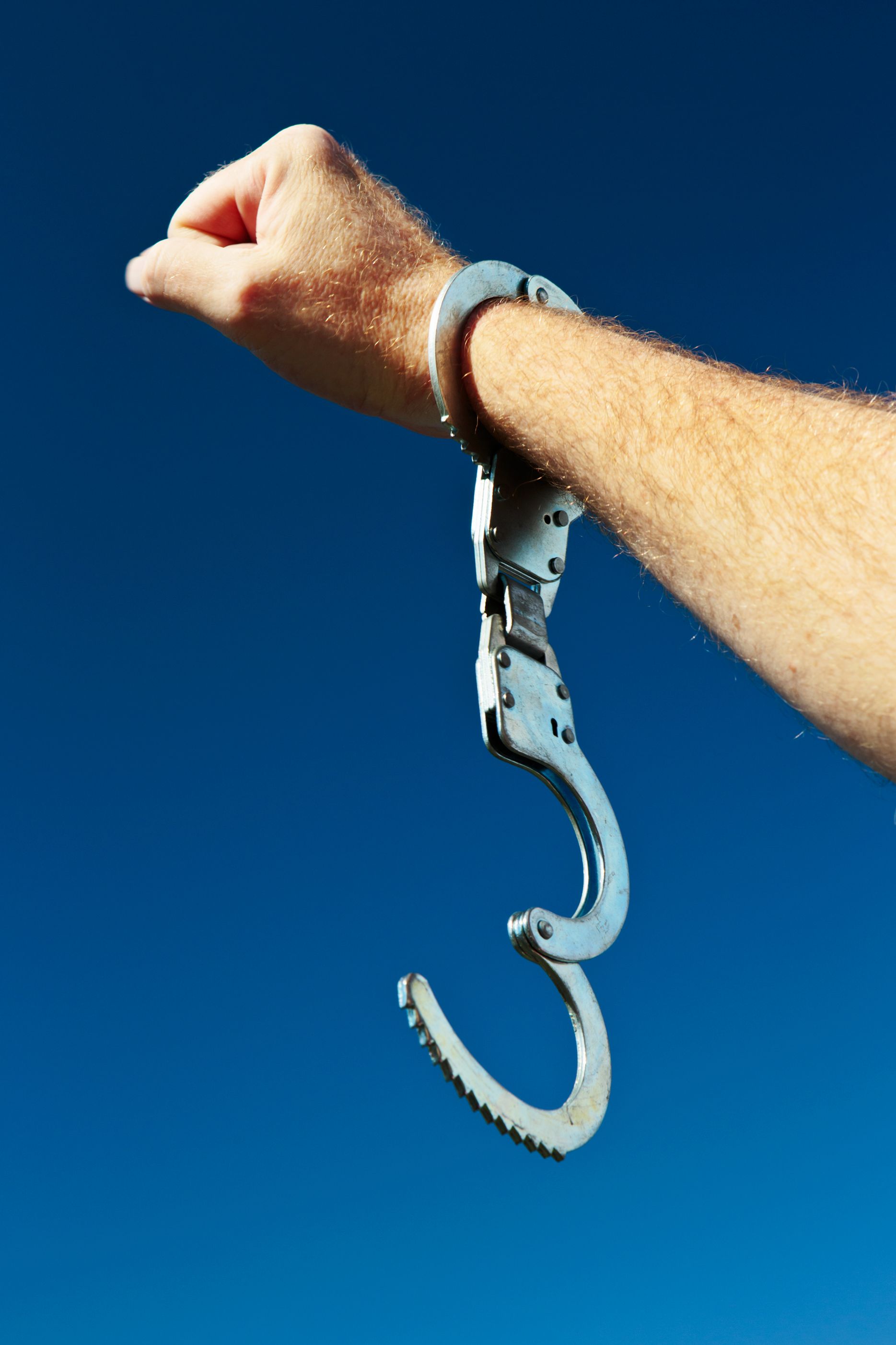 A man's hand, holding up a clenched fist in a salute, and wearing a single, open handcuff.