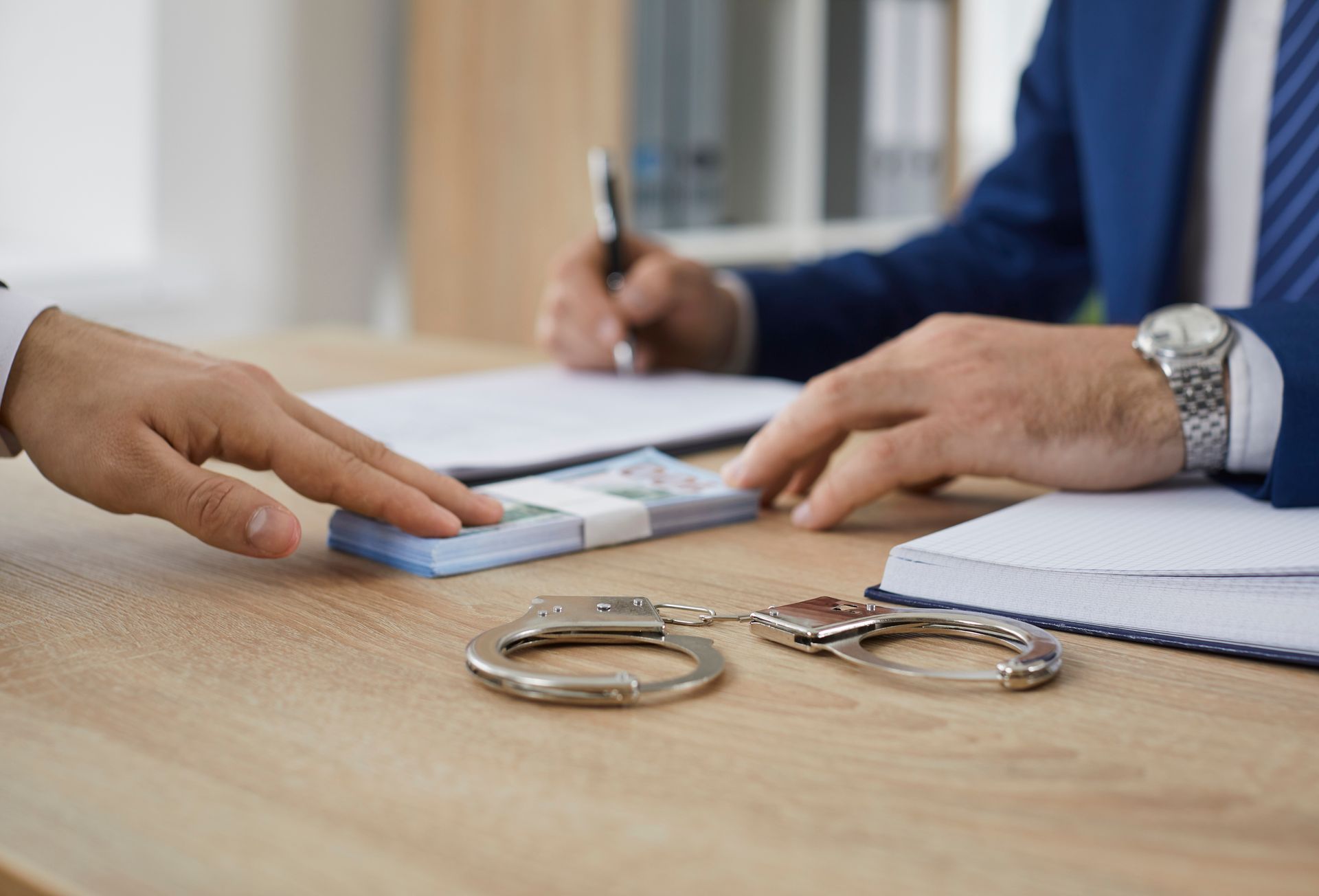 Bondsman signing paperwork with client, handcuffs on table, legal documents.