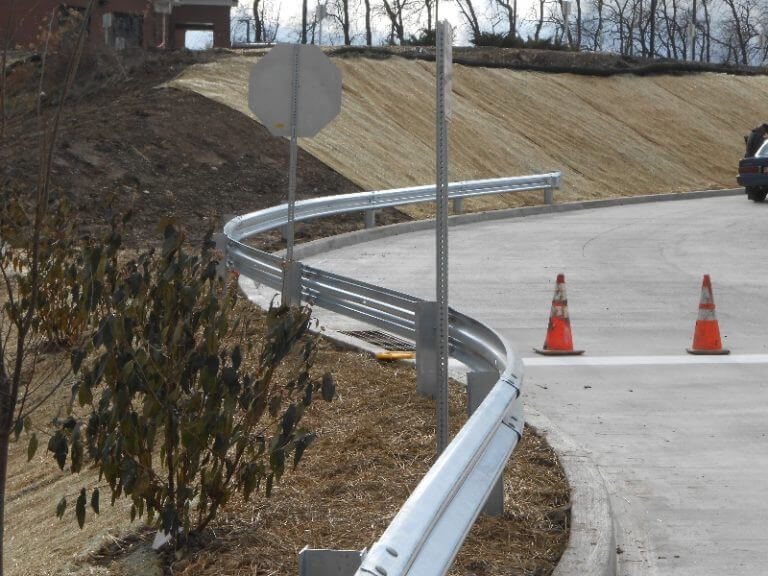 Curving roadside guardrail beside a concrete ramp with orange traffic cones and a stop sign on a slope