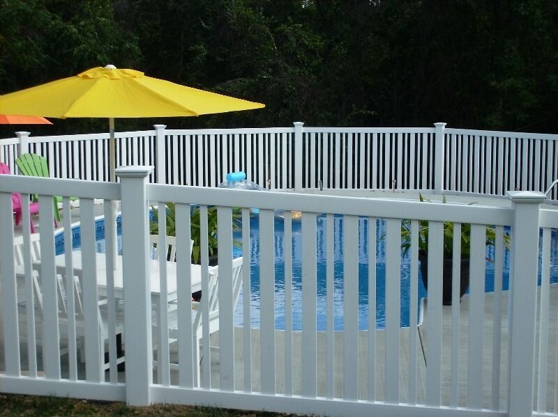 Backyard pool with yellow umbrella, white fence, and blue chairs under a cloudy sky