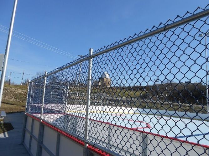 Chain-link fence beside an outdoor ice rink under a clear blue sky