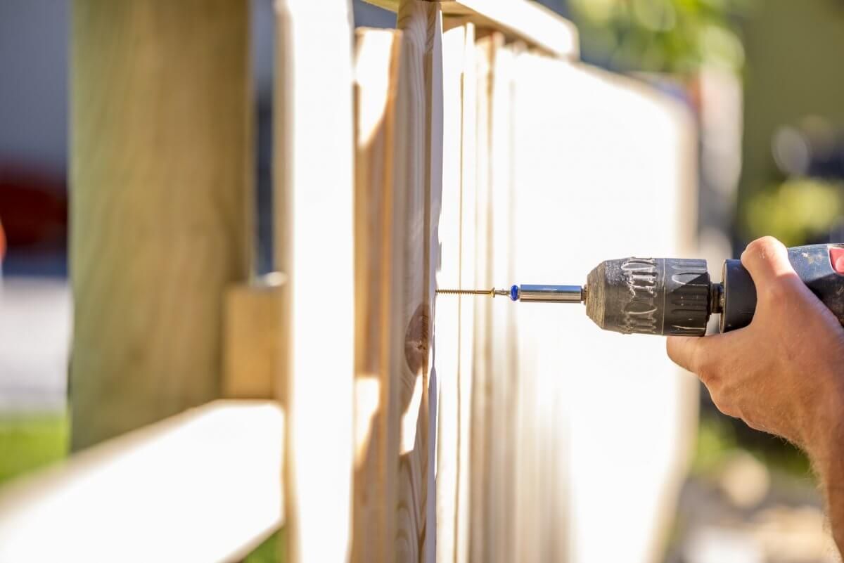 Hand drilling a hole in a wooden fence panel outdoors in sunlight