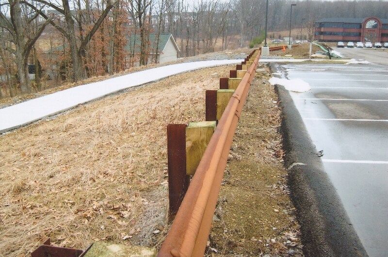 Rusty guardrail beside a snowy roadside and empty parking lot in a wooded area