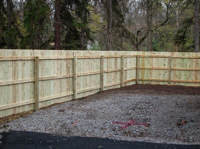 Wooden privacy fence enclosing a gravel yard with trees in the background