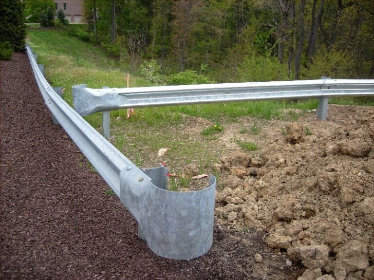 Damaged metal roadside guardrail bent into a ditch beside gravel and dirt embankment