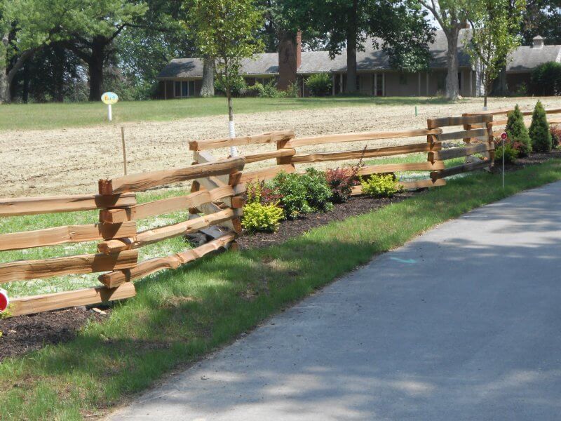 Wooden split-rail fence along a grassy path with small shrubs and trees in a park
