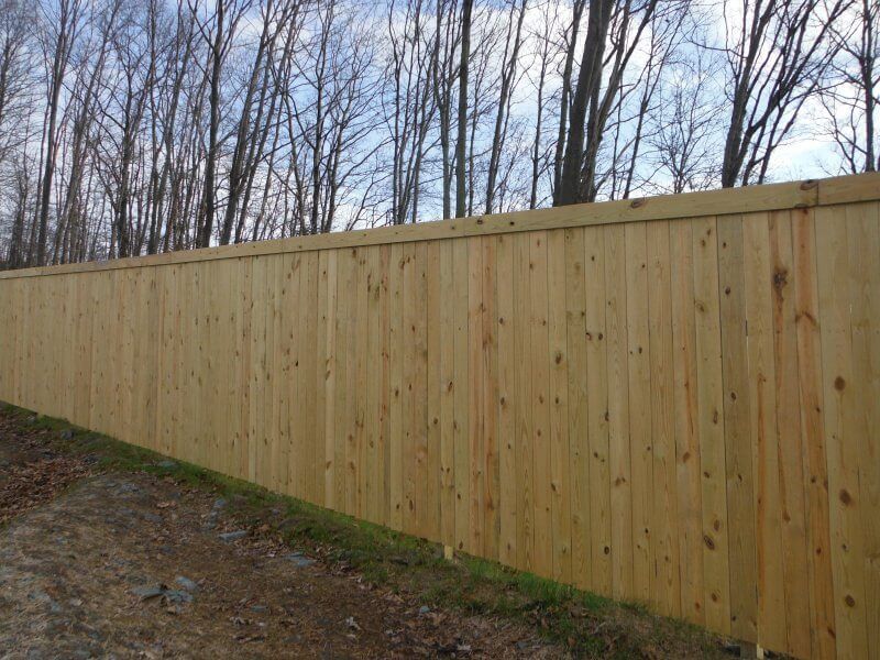 Long wooden privacy fence along a dirt path beside leafless trees