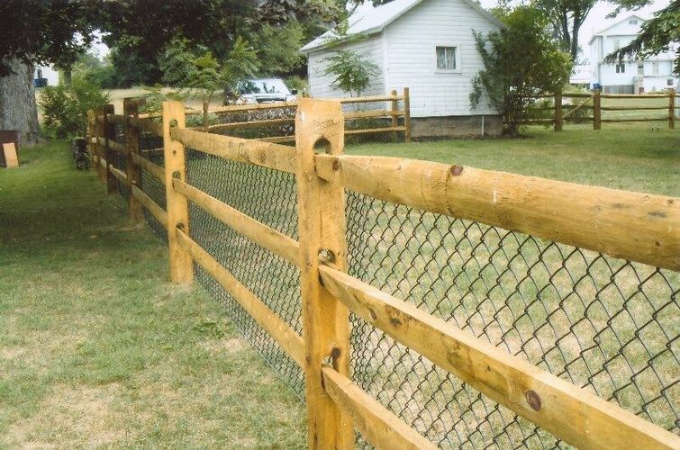 Wooden and chain-link fence beside a grassy yard with a white house in the background