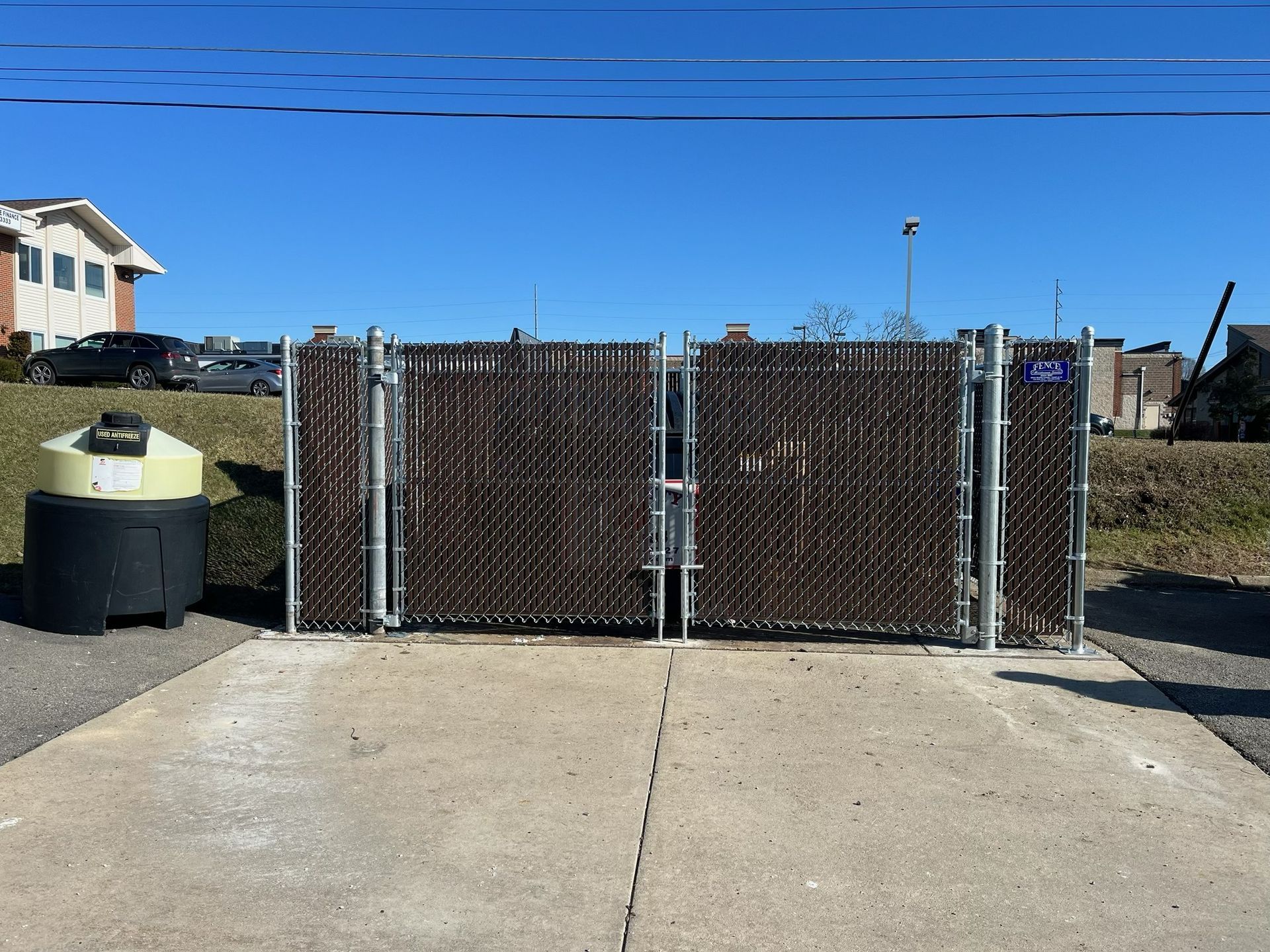 Chain-link gate between concrete driveway and open lot under a clear blue sky.