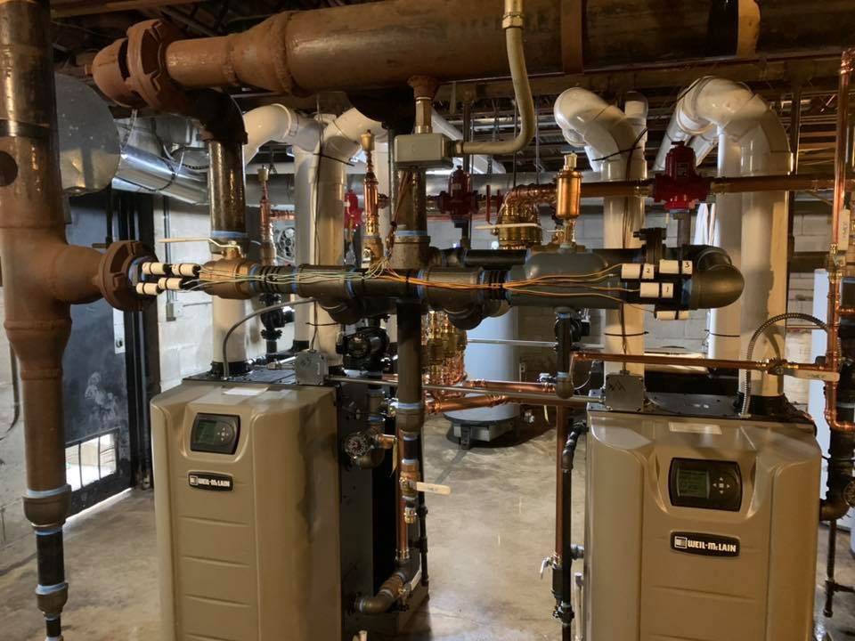 The image displays a commercial heating system featuring two Weil-McLain high-efficiency condensing gas boilers. The image displays a commercial heating system featuring two Weil-McLain high-efficiency condensing gas boilers.