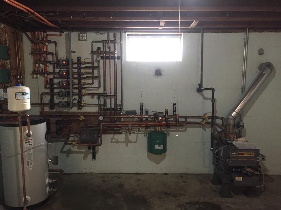 The image displays a residential boiler room or mechanical room, which houses the equipment for a hydronic (hot water) central heating system. 