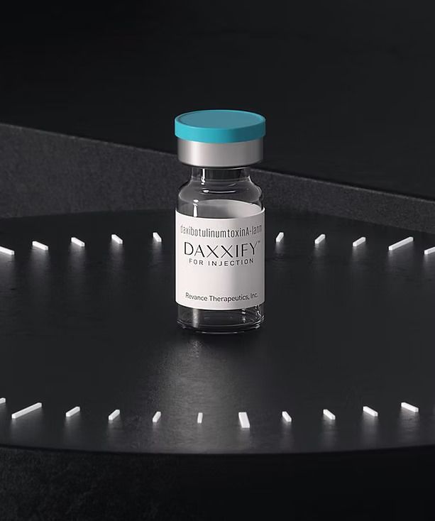 Vial of DAXXIFY botulinum toxin for injection on a black surface with a teal and silver cap.
