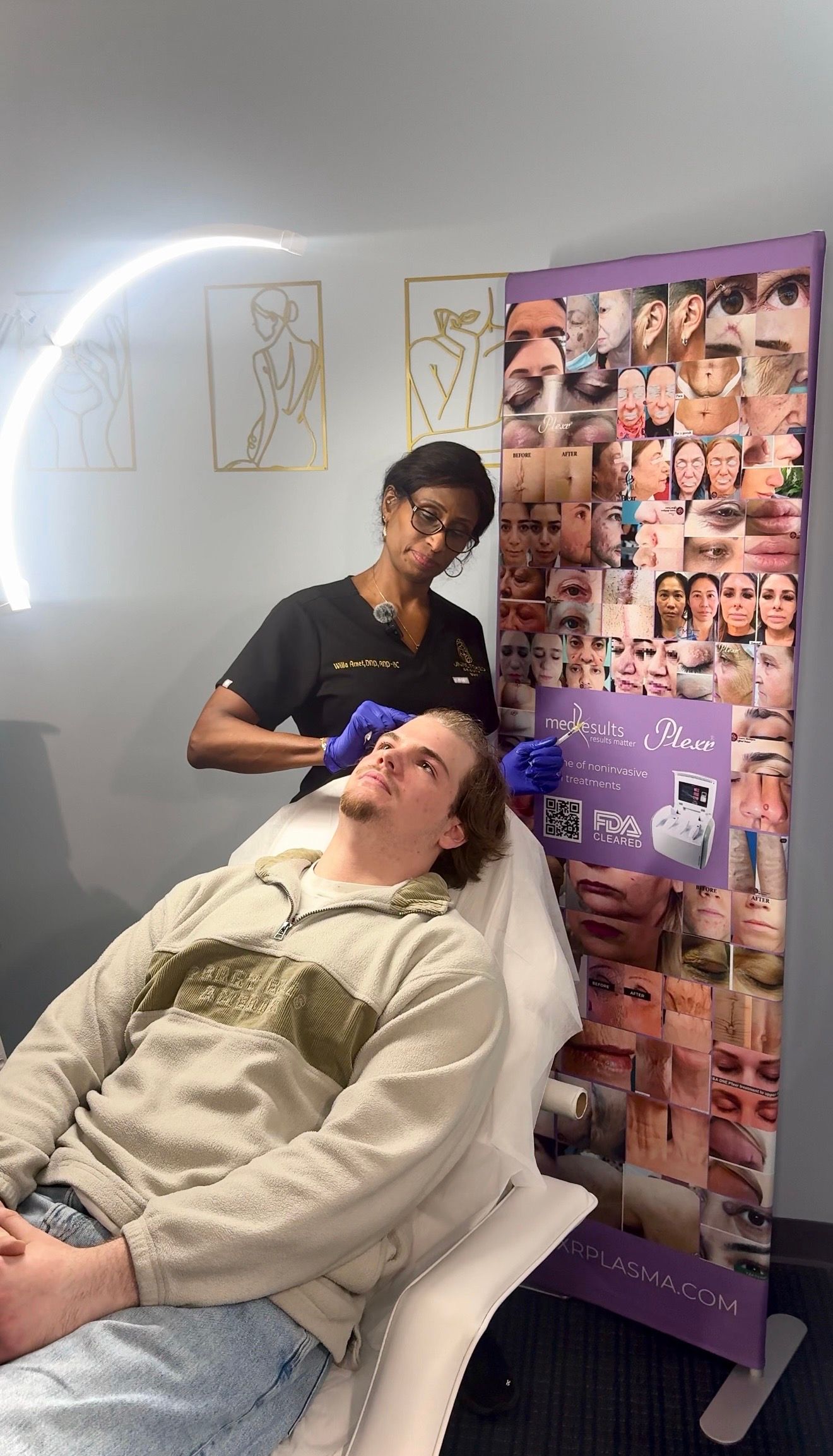 A professional wearing gloves and a white coat examines a person’s scalp in a brightly lit clinical setting.