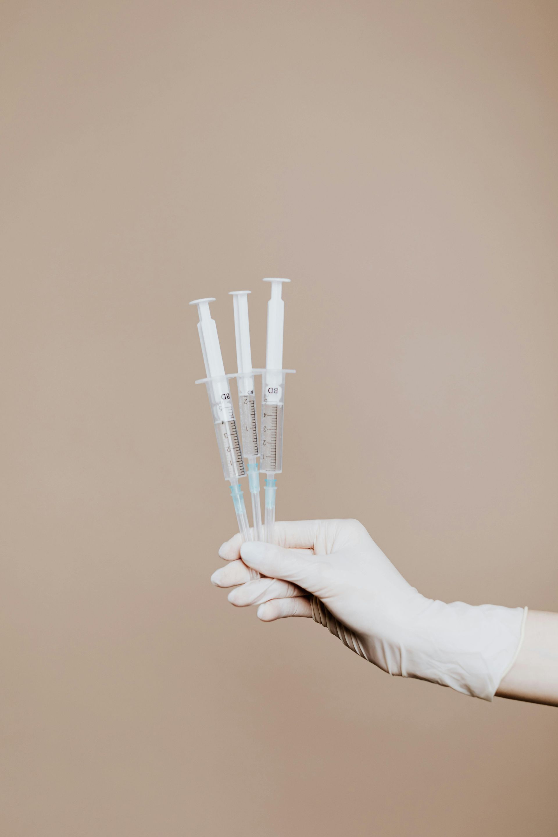 Gloved hand holding three syringes against a neutral background.
