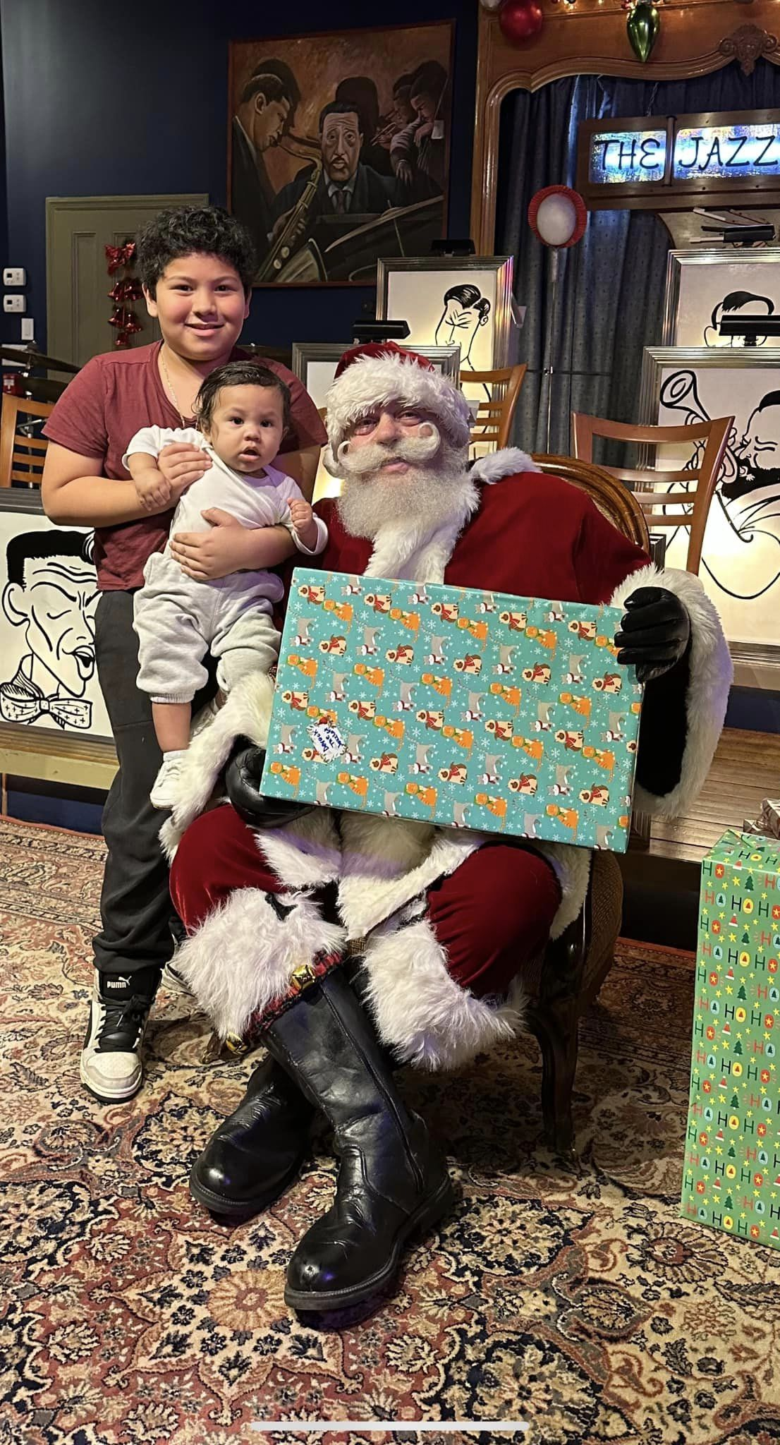 A woman is holding a baby while sitting next to santa claus.