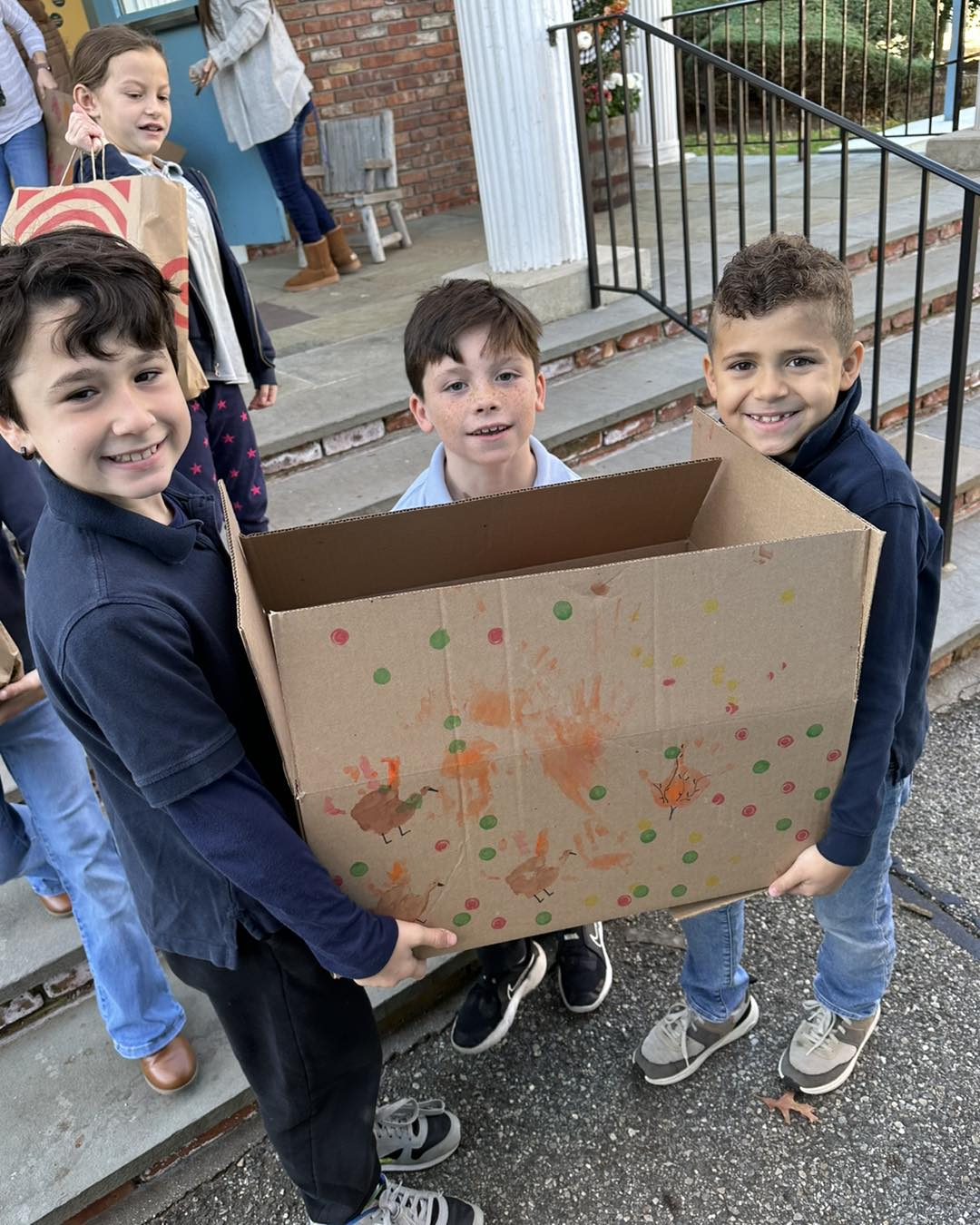 Three young boys are holding a cardboard box in front of a building.