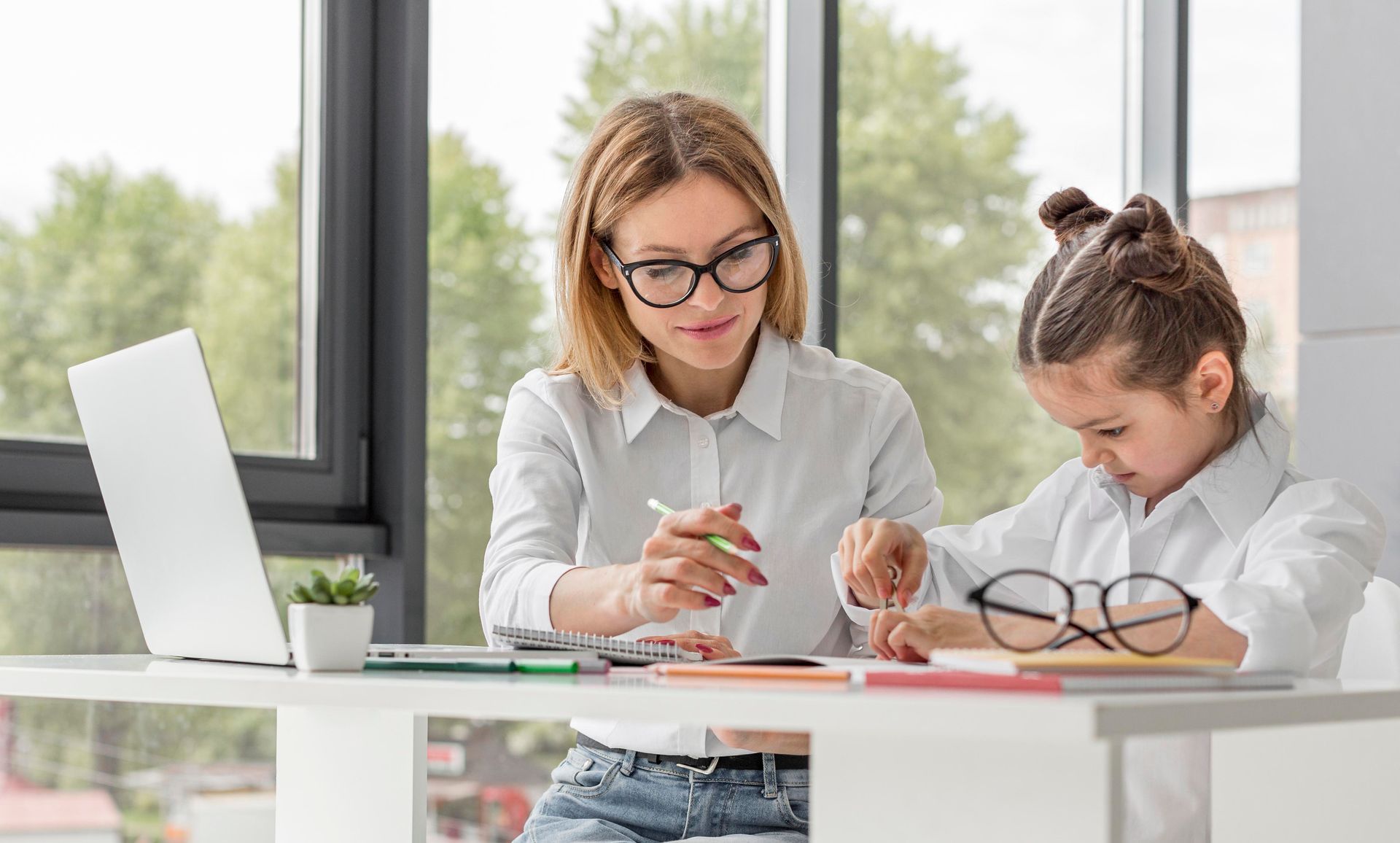 A woman and a little girl are sitting at a table with a laptop.