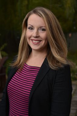 A woman wearing a pink and black striped shirt and a black jacket is smiling for the camera.