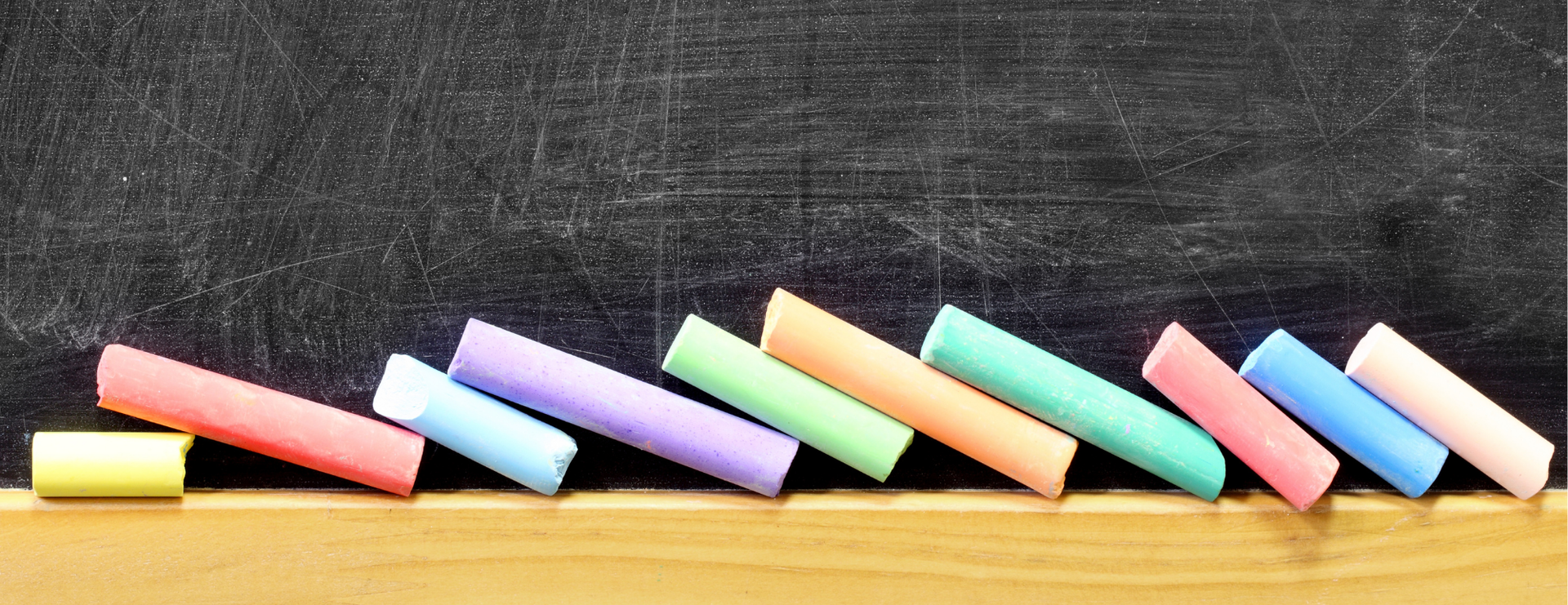 Chalkboard with colourful chalk leaning on a wooden ledge.
