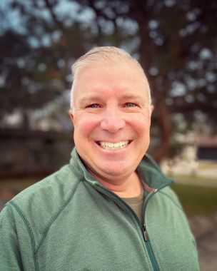 A man in a green jacket is smiling for the camera.