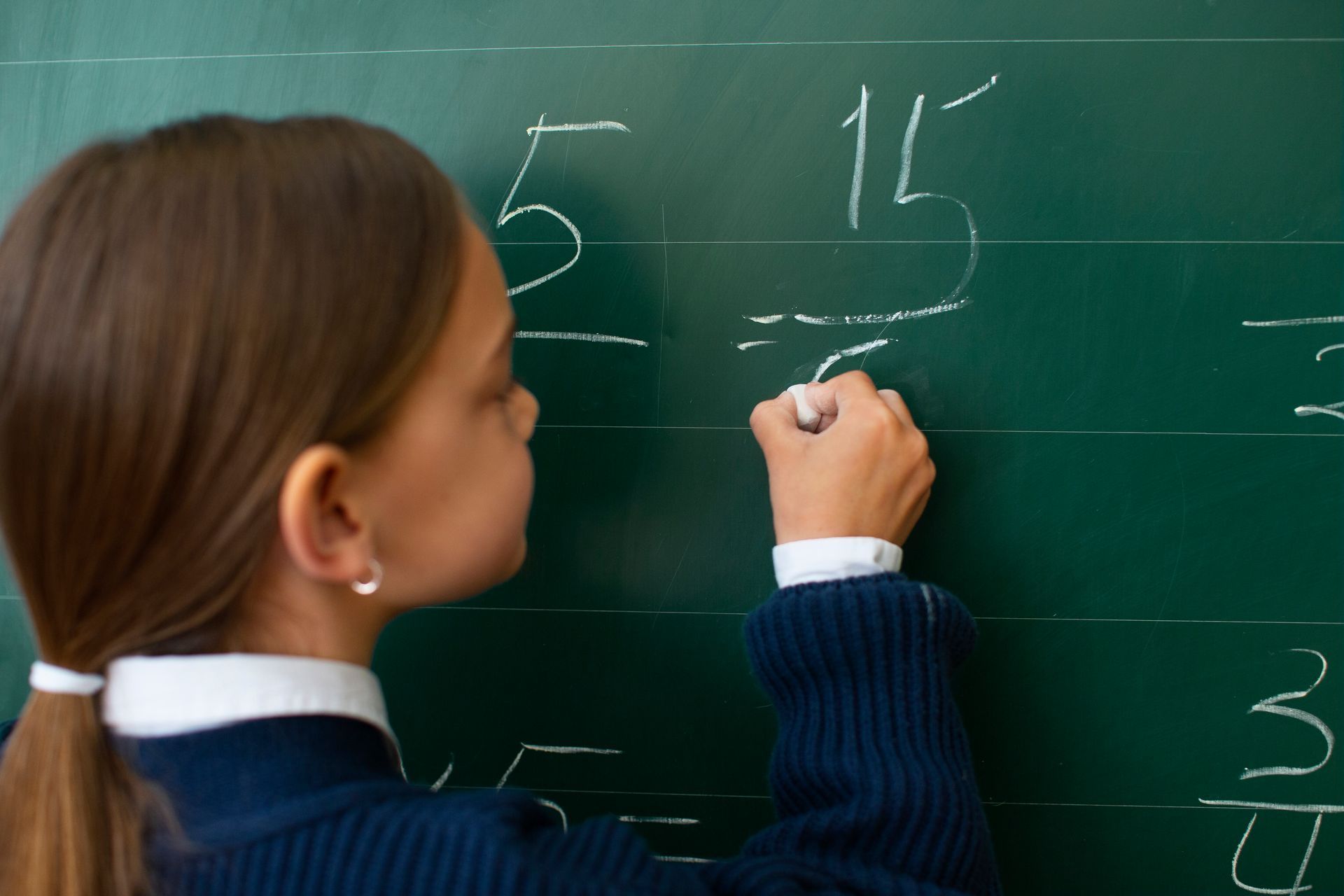 A girl is writing on a green board with chalk