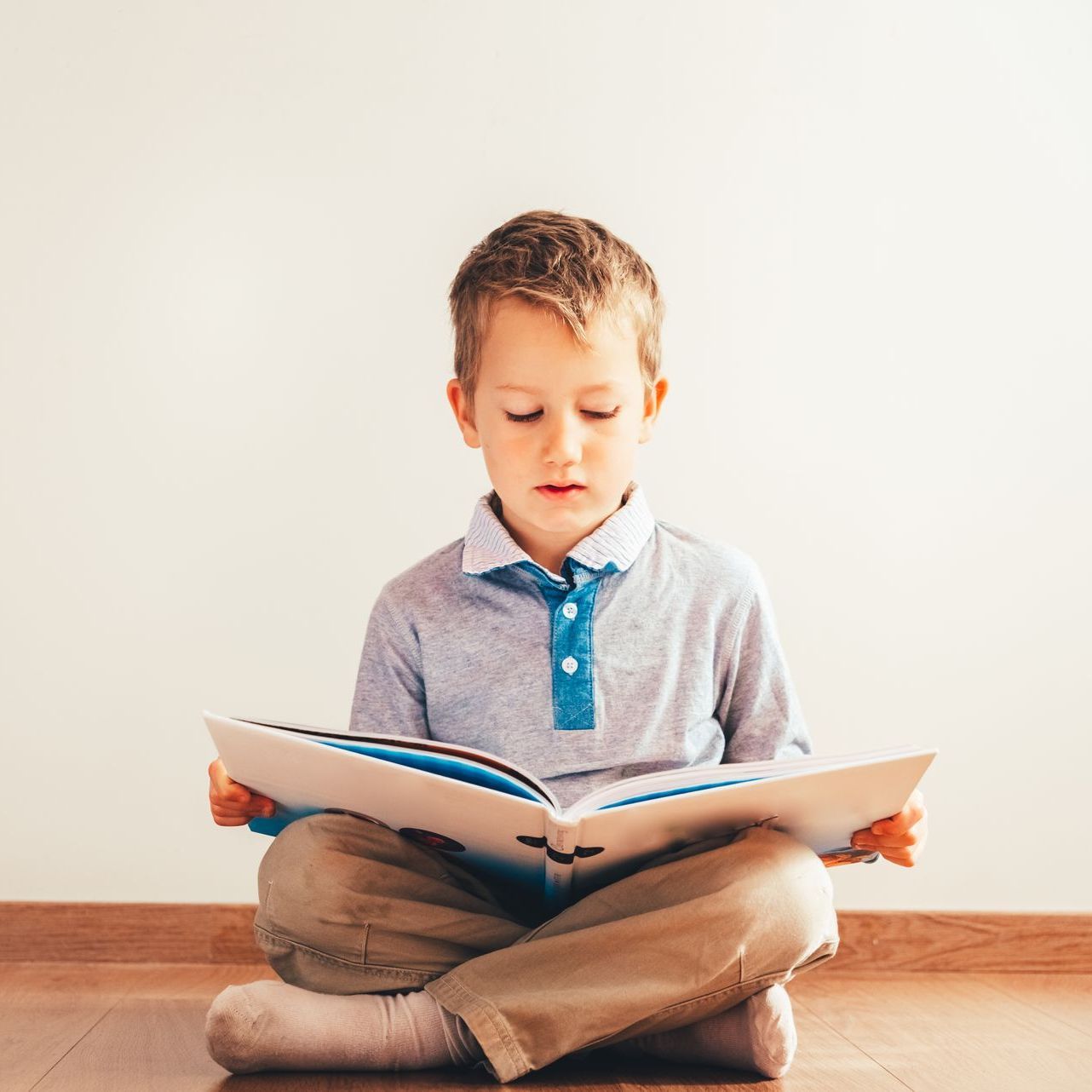 A young boy is sitting on the floor reading a book.