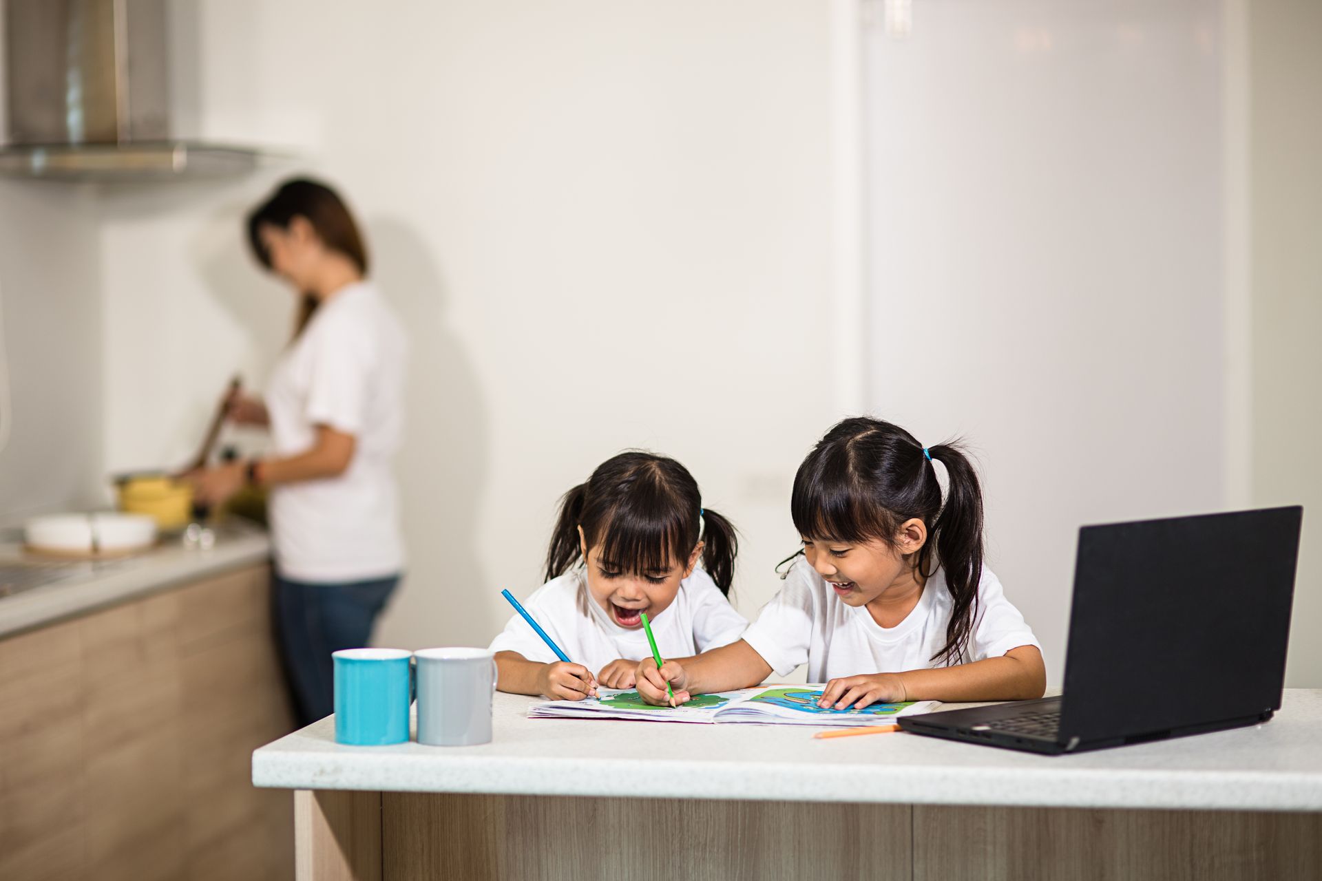 Two little girls are sitting at a table with a laptop.