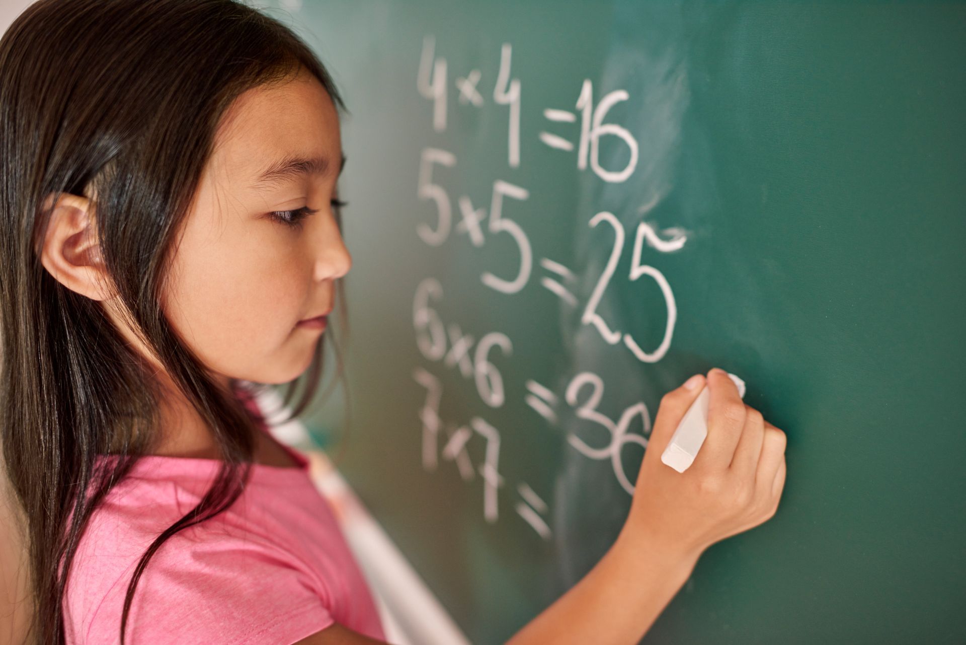 A young girl is writing on a blackboard with chalk.