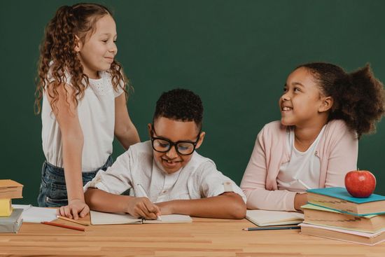 A group of children are sitting at a table with books and an apple.