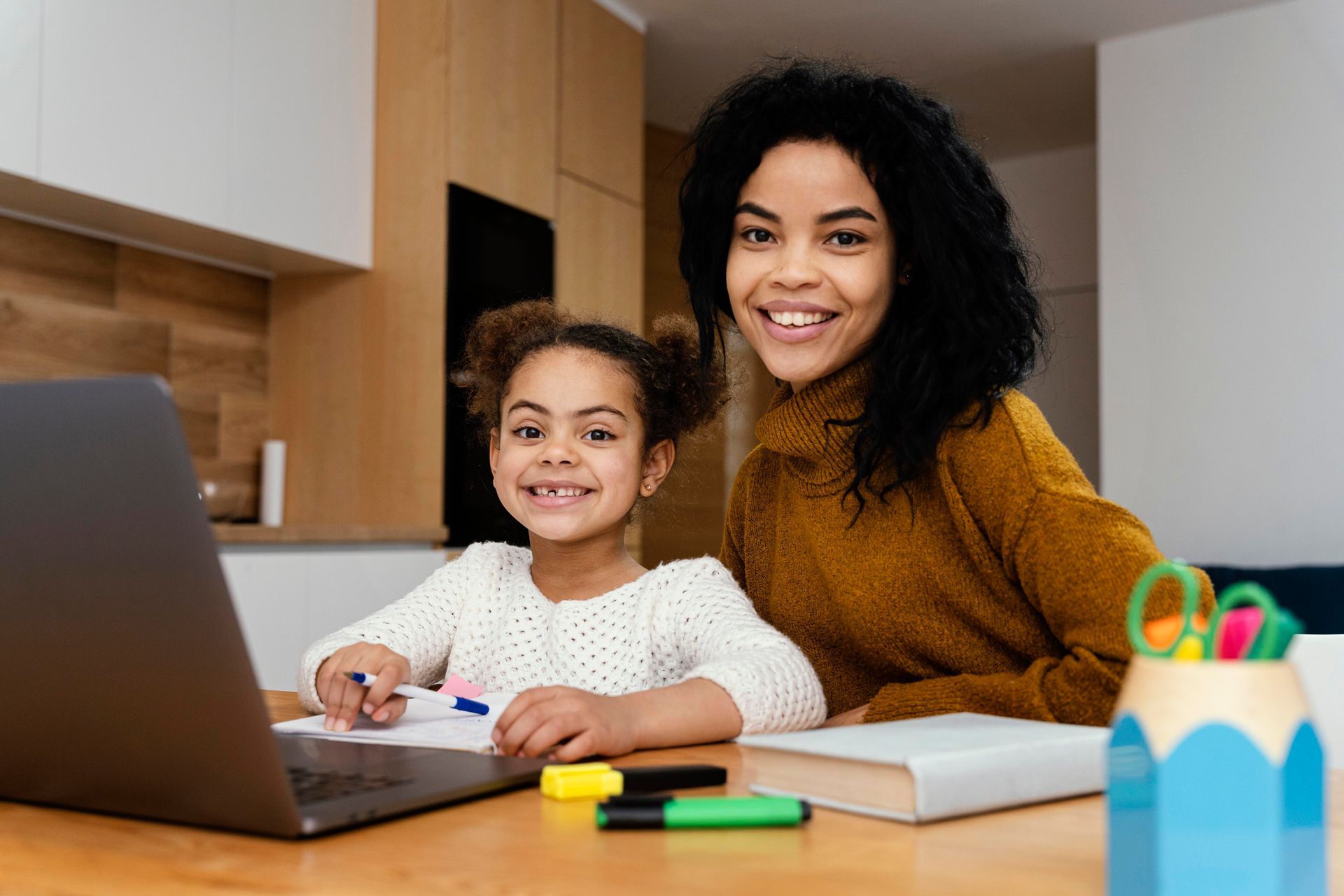 A woman and a little girl are sitting at a table with a laptop.