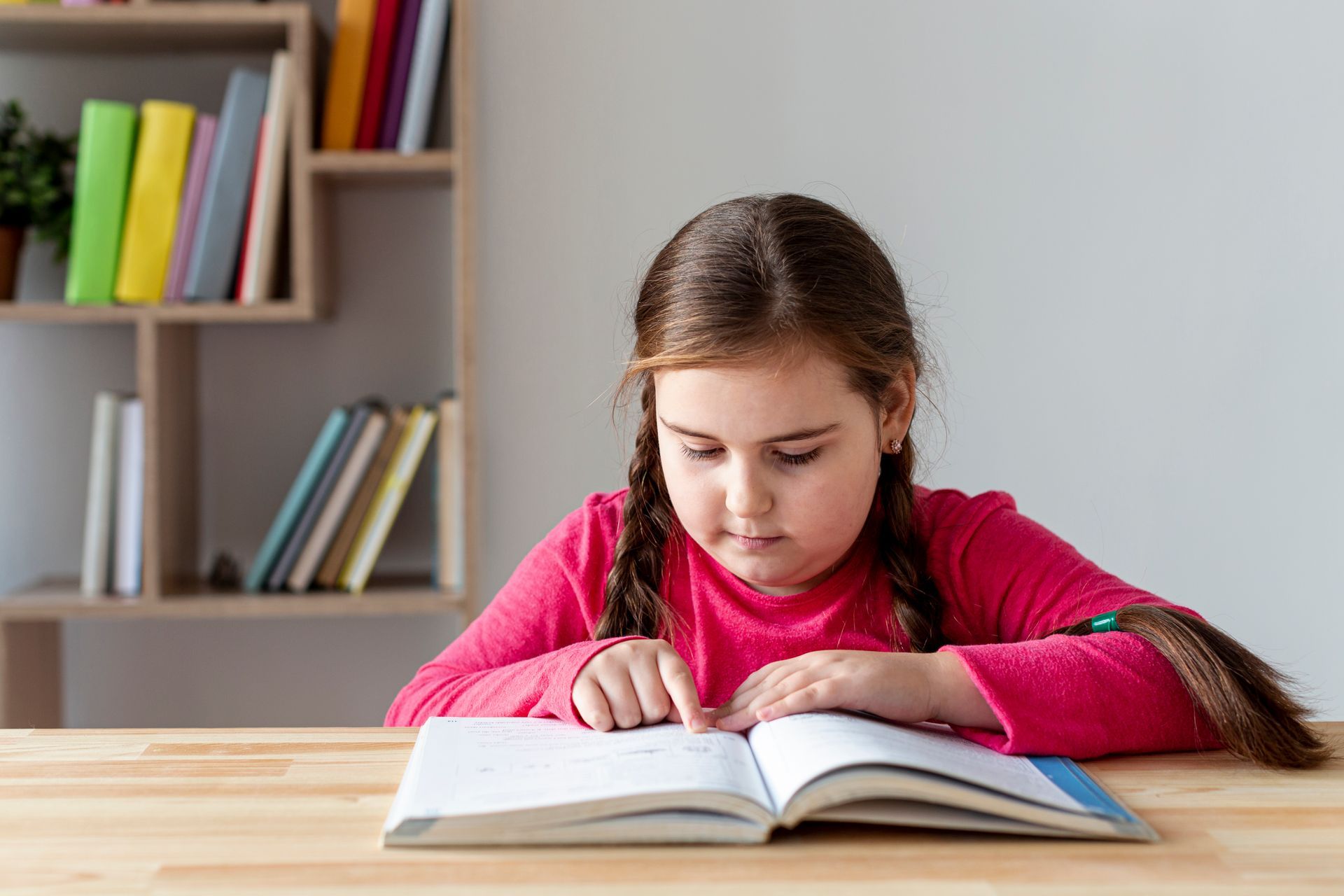 A little girl is sitting at a table reading a book.
